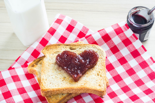 Breakfast toast with red heart jam symbol on a red checkered table cloth.